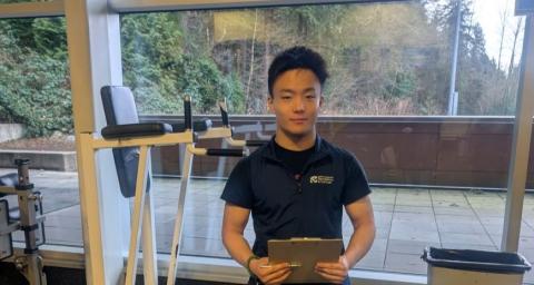 A practicum student holding a clip board and wearing an NVRC vest works in the Delbrook Fitness Centre.