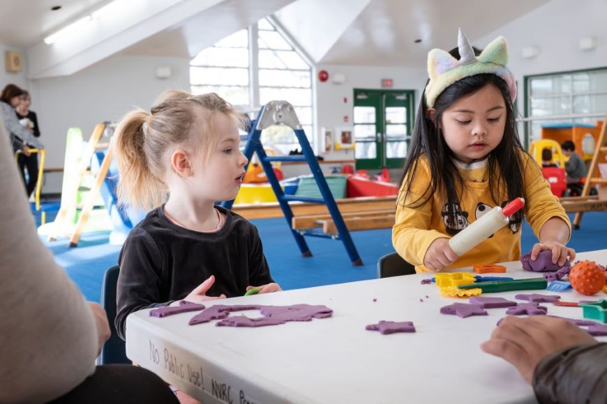 Play-Doh, climbing equipment and toys! Two toddler girls play with Play-Doh and toys on a table, with a play room and parents in the background.