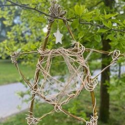 Stars of the Neighbourhood A woven willow star hangs from a leafy tree branch in a park.