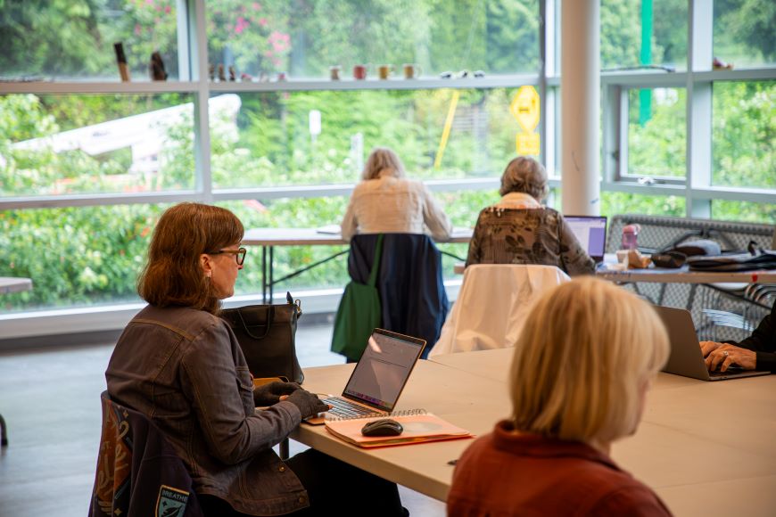 Silent Writers Workshop A group of women work on laptops at tables in a room with large windows.
