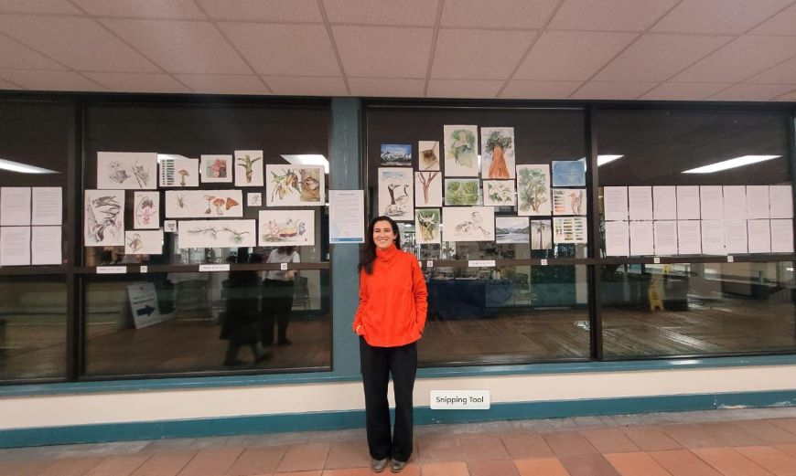 A woman in a red sweater stands in front of an art display pasted on large windows. 