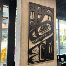 This powder-coated aluminum piece depicts a killer whale through bold cut-out forms that reveal the concrete pillar behind it.