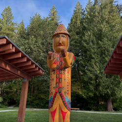 Contemporary Coast Salish welcome figure with raised hands, carved from cedar in a park. 