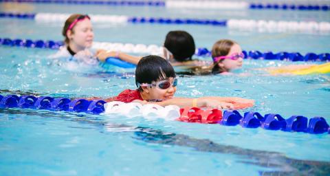 Children practice their strokes in the pool with a swim instructor.
