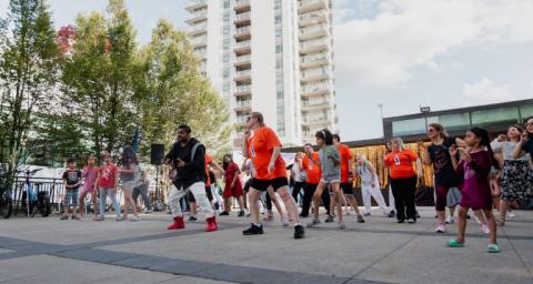 Community members of all ages learn bollywood dance moves in a public plaza.