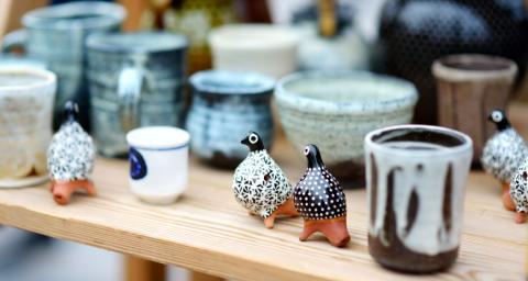 Handmade pottery items, including mugs, bowls, cups, and quail-shaped salt shakers are displayed on a wooden shelf. 