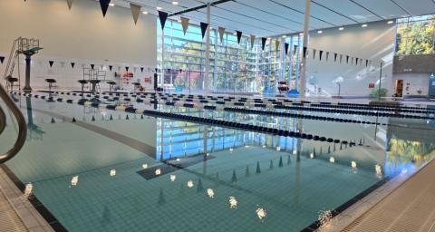 A lane swimming pool with flags strung over top and a diving board at one end. 