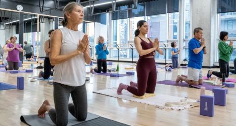 People kneel on mats on a wood floor during a yoga class