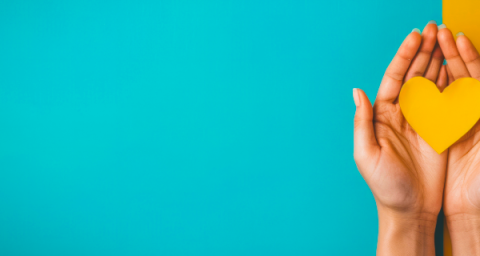 A pair of hands holding a yellow paper heard against a turquise and yellow background