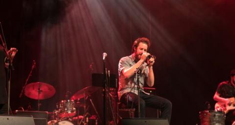 A band consisting of two vocalists and an electric guitarist play on a stage. 