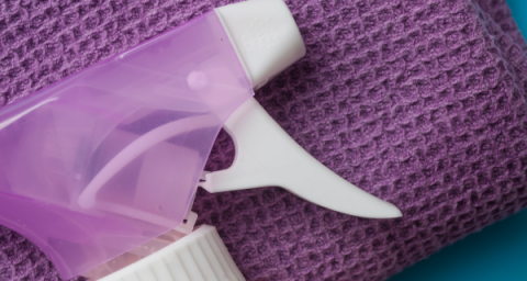 A folded purple cloth towel, with a white and purple spray bottle resting on top. 