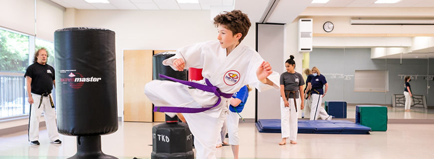 child kicking a target in taekwondo class