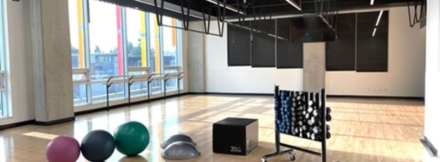 The workout studio at the Lions Gate Community Recreation Centre offers large windows and lots of natural light. Also pictured is the range of handheld fitness equipment available for studio workouts, including BOSU balls, foam rollers, resistance bands, and dumbbells. 