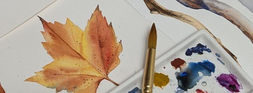 An artist's watercolour works in-progress on a table, including a palette and brush, colour swatches, and paintings of a leaf and branches are visible. 