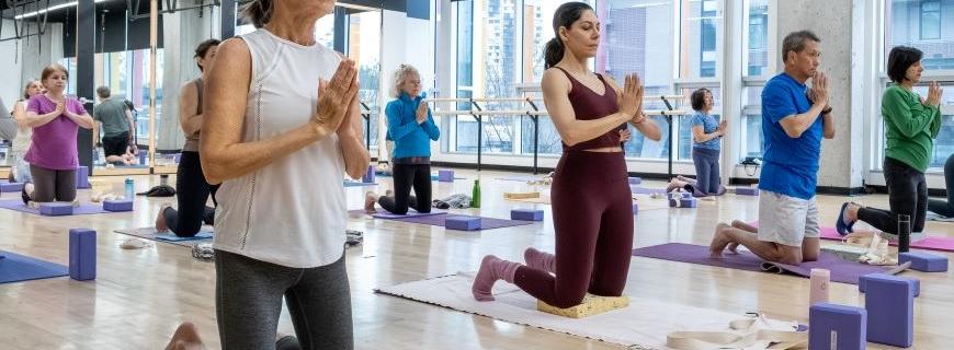 People kneel on mats on a wood floor during a yoga class