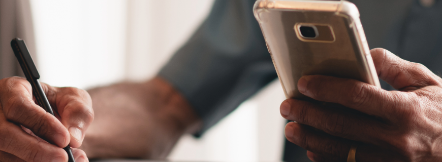 A man holds a phone while writing a list with the other.