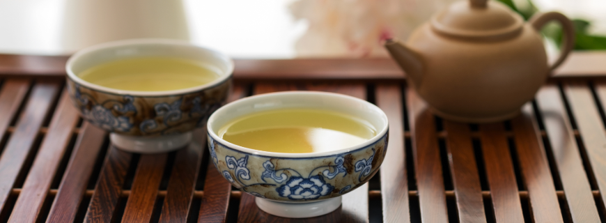 Two tea cups and a tea pot on a wooden tray