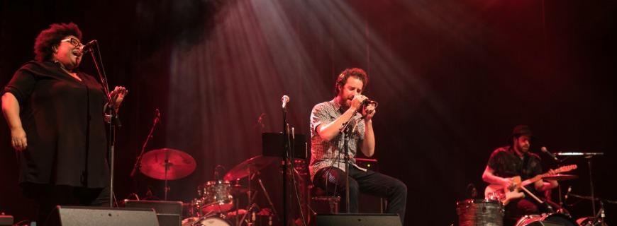 A band consisting of two vocalists and an electric guitarist play on a stage. 