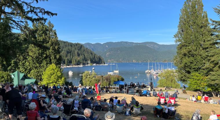 Audience members watching performers in Deep Cove with ocean and mountain back-drop.
